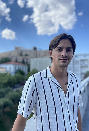 Julian posing outside, wearing a white shirt with blue vertical stripes.