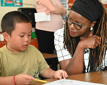 Dr. Charlene Williams sitting with a student in a classroom.