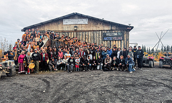 A group photo of the attendees beneath the Arctic Village sign.