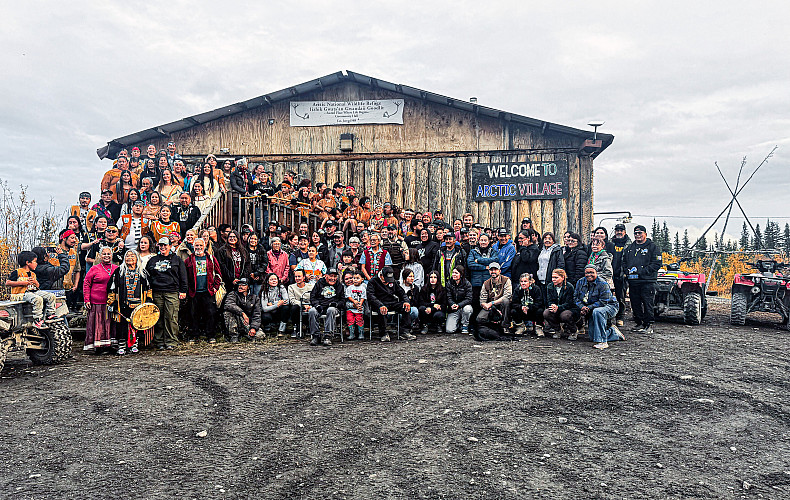 A group photo of the attendees beneath the Arctic Village sign.