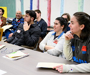 Students sitting together at a table, smiling at the teacher.