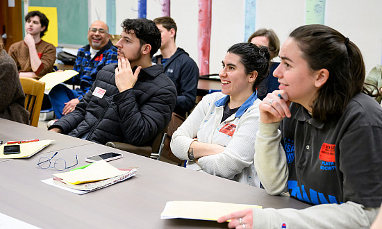 Students sitting together at a table, smiling at the teacher.